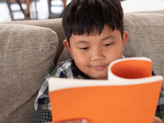 Cute asian children reading a book while lying on a sofa in the room. education concept