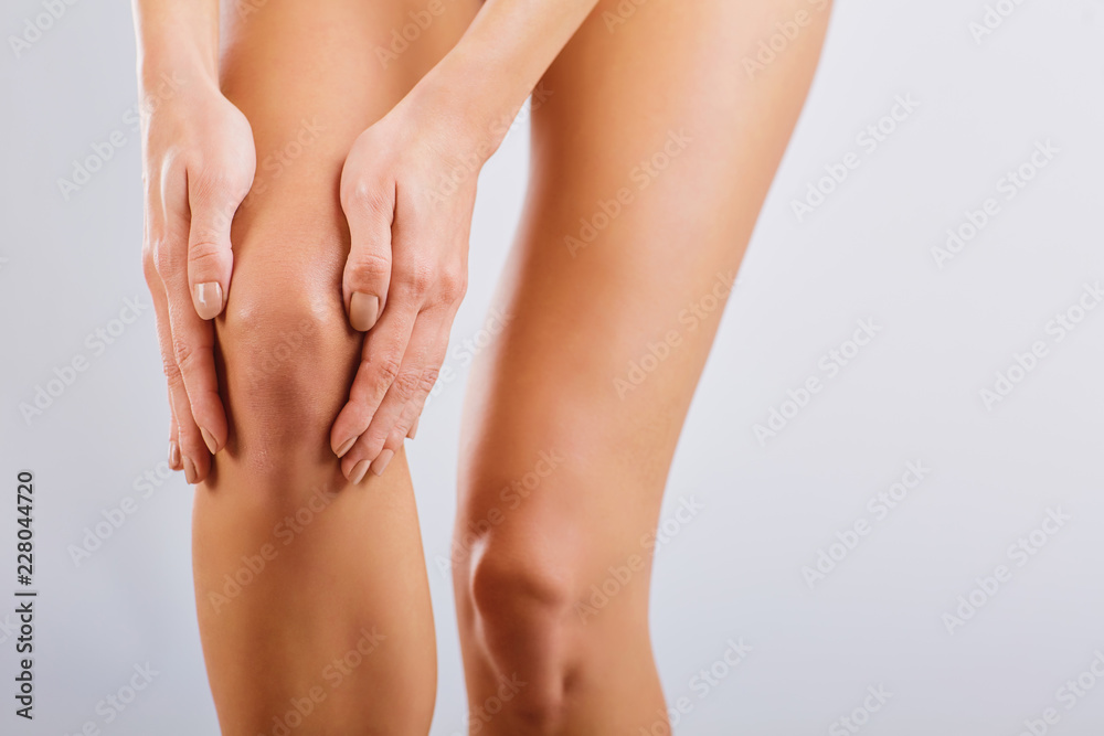 Pain, injury to the knee. A woman holds her knee with her hand. - obrazy, fototapety, plakaty 