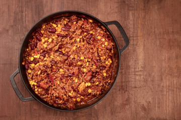 Wall Mural - A large cast iron pan with chili con carne, shot from the top on a dark rustic wooden background with copy space