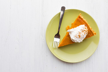 Slice of pumpkin pie with whipped cream over white wooden background