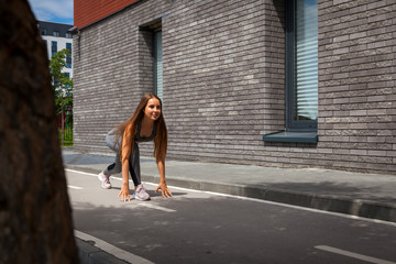 Wall Mural - Young woman gymnast with a slim figure in sportswear doing stretching on a city street on a warm summer day. Stretching in the open air