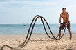 Young man training with battle ropes on the beach