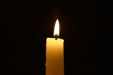 standing wax lighting candle with big fire on the dark background.