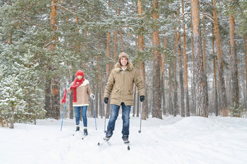 Wall Mural - Full length portrait of modern active couple enjoying skiing in snowy winter forest during date, copy space