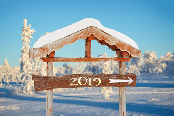 Wall Mural - 2019 written on a wooden direction sign, blue sky and snowy landscape background