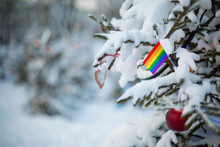 LGBT Flag. Christmas Background Outdoor. Christmas Tree Covered With Snow And Decorations And Rainbow Flag.  New Year / Christmas Holiday Greeting Card.