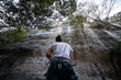 © pablobenii - From below of anonymous man in harness looking up at mountain and checking partner climbing cliff