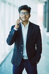 Indian businessman talking on phone in front modern office building.