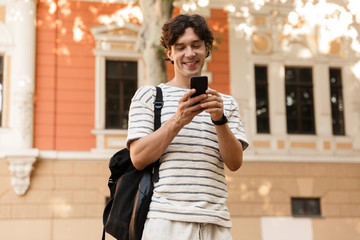 Wall Mural - Cheerful man posing outdoors on the street using mobile phone.