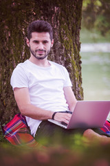 man using a laptop computer on the bank of the river