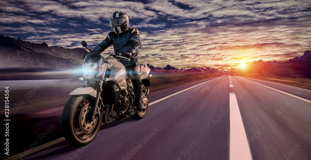 motorcyclist rides home in the evening on a highway while sunset - obrazy, fototapety, plakaty 