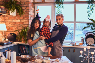 Wall Mural - Mom dad and little daughter with makeup and hats cooking together in loft style kitchen at morning.