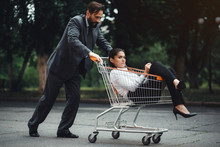 Business Woman Sitting In Cart. Her Male Colleague Pushing Her. Being Outside.