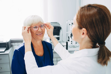 Wall Mural - Happy senior woman trying out new reading glasses at optician office