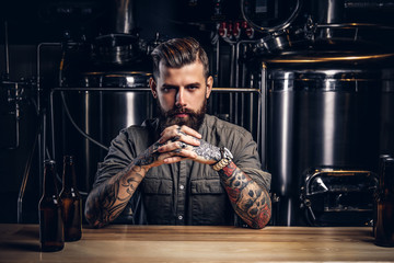 Portrait of a pensive tattooed hipster male with stylish beard and hair in the shirt in indie brewery.  