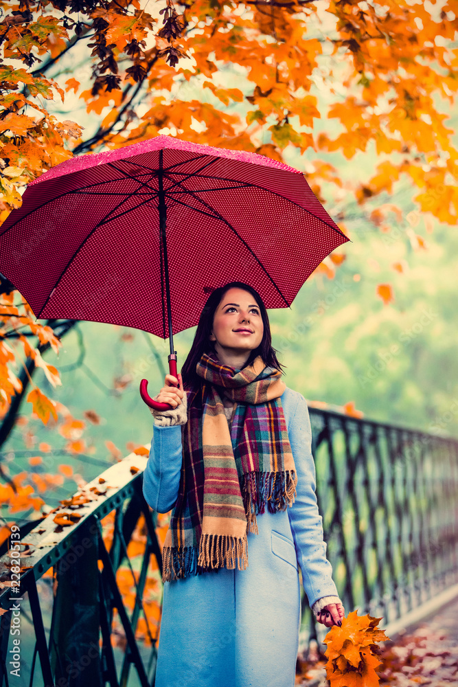 Young beautiful brunette girl in blue coat with umbrella walking in the autumn park - obrazy, fototapety, plakaty 