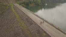 Aerial View Of Three Bicyclist Biking Over The Dam In Colibita Lake, Romania, During Tura Cu Copaci  Bike Race.