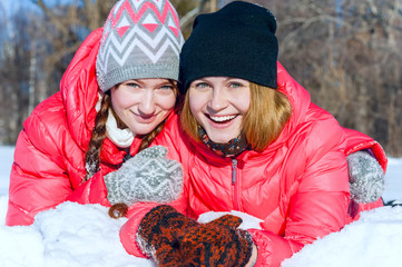 Outdoor portrait of two young happy smiling girl lying on the snow in winter park