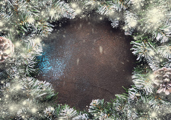 Christmas or New Year frame composition with  green snow fir branches, pine cones, golden snowflakes, Christmas balls, red berries, and alarm clock on brown background, top view