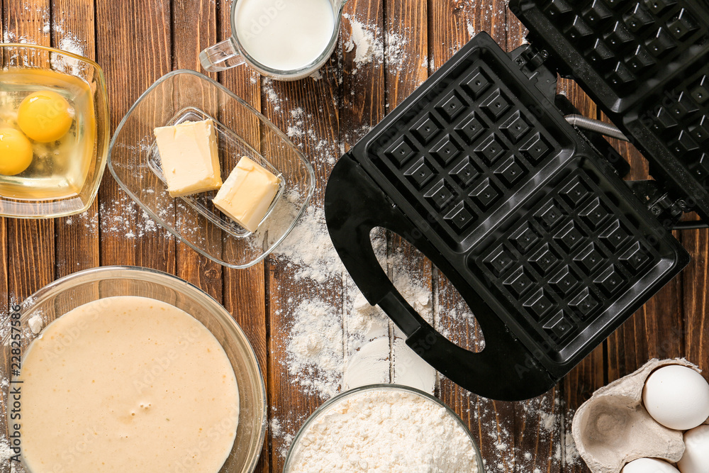 Modern waffle maker with ingredients on wooden table