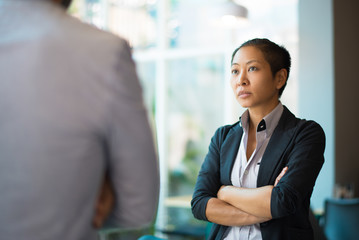 tense asian businesswoman looking at male partner with crossed arms. two colleagues confronting each