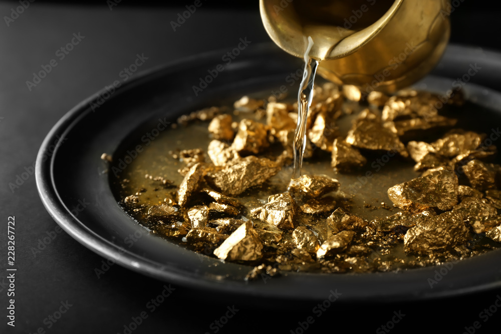 Pouring of water on plate with gold nuggets