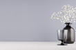 Perfect stylish home festive decoration in grey colors - black glass goblet and vase with small fluffy flowers on soft ligth white wood table.