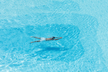 Aerial  view on the men in the swimming pool with transparent blue water. In the motion