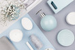 Fashion art cosmetics flat lay of different cosmetics products and accessories of silver, pastel blue and white color with small flowers on paper and white wooden background.