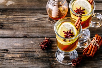 Wall Mural - Hot spiced Apple cider Toddy with lemon, honey and cinnamon stick in glass on wooden background