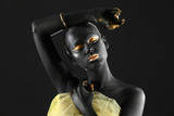 Fototapeta  - Beautiful woman with black and golden paint on her body against dark background