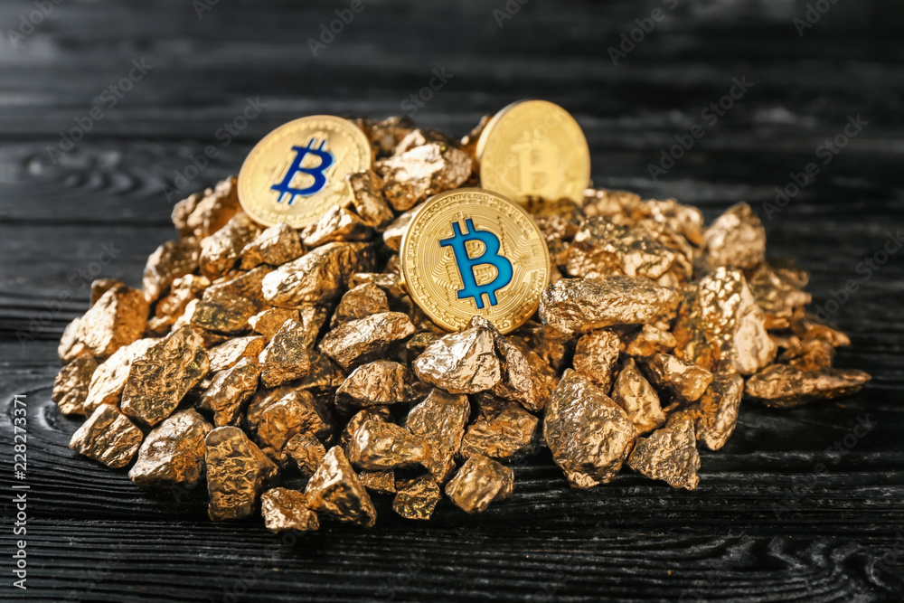 Gold nuggets and bitcoins on dark wooden background