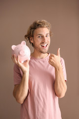 Sticker - Happy young man with piggy bank on color background