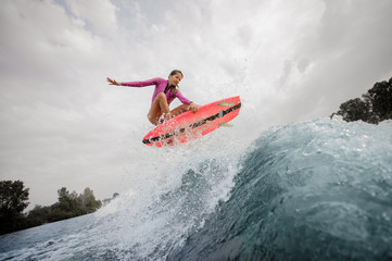 Wall Mural - Active and young woman wakesurfer jumping up the blue splashing wave against sky