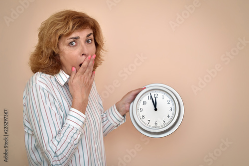 Fotografie, Obraz Surprised and scared middle aged woman holding a big clock