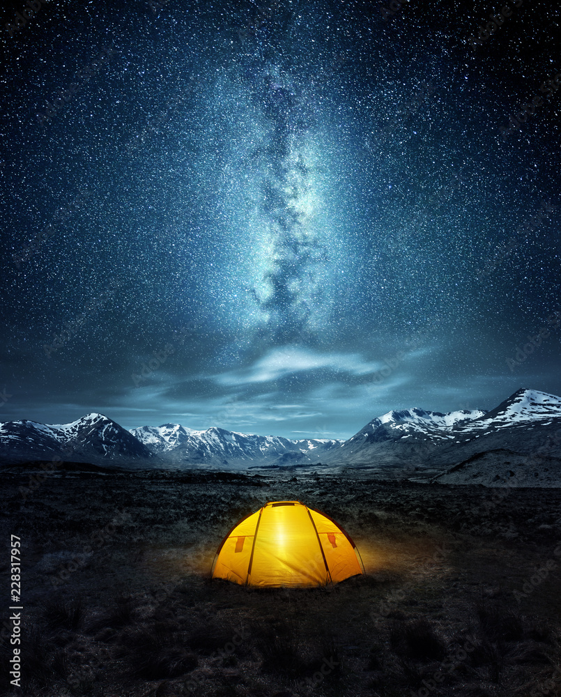 Camping in the wilderness. A pitched tent under the glowing  night sky stars of the milky way with snowy mountains in the background. Nature landscape photo composite. - obrazy, fototapety, plakaty 