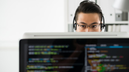 Young Asian man in headset and glasses working with computer and programming