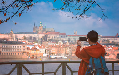 Back view of young man takes pictures by cellphone with a beautiful landscape of the world famous Prague landmark with blue sky in the autumn season