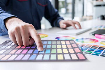 Poster - Male creative graphic designer working on color selection and color swatches, drawing on graphics tablet at workplace with work tools and accessories