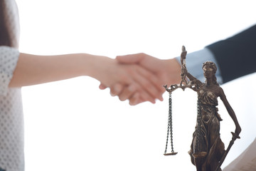 Wall Mural - close-up view of lady justice statue and lawyer with client blank shaking hands behind