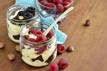 Wall Mural - Dessert with chocolate biscuit, cream, hazelnut and fresh berries in glass jars, trifle, copy space
