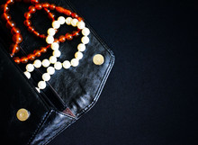 Jewelry In A Woman's Handbag. Beads Of Pearls And Amber On A Black Background. Black Clutch With Beads. A Lady's Purse.