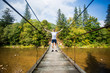 © Svetlana - Tourist man walk by long wooden suspension bridge above river. balance concept