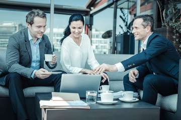 Wall Mural - Look here. Handsome male person keeping smile on his face and pointing at computer while sitting in semi position