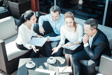 Wall Mural - Project presentation. Cheerful brunette lady keeping smile on her face and holding folder on knees while looking at her partners