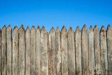 Fence Made Of Sharp Wooden Stakes Against The Blue Sky. Wooden Fence Vertical Logs Pointed Against The Sky Protection Against Invaders And Wild Animals