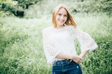 Beautiful attractive young woman posing in spring park wearing white knitted top and blue jeans, modern creative toning