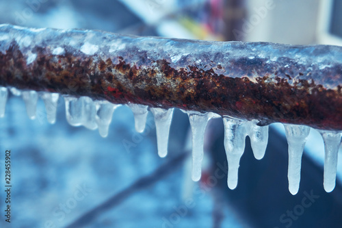 Many small icicles have frozen on a rusty pipe in the street in the winter Poster Mural XXL