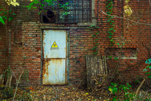 The Entrance In The Old Abandoned Industrial Building With The Yellow Triangle Danger Sign With Black Skull And Bones