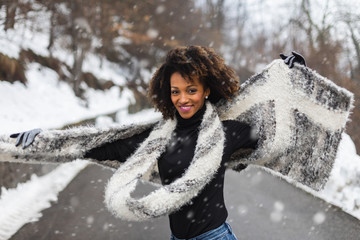 Young black woman dancing and having fun under the snow in cold winter.